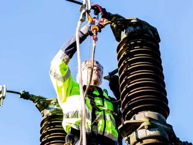 Szakember hi-vis védőfelszerelésben kábelvégzárást szerel egy villamos oszlopon
